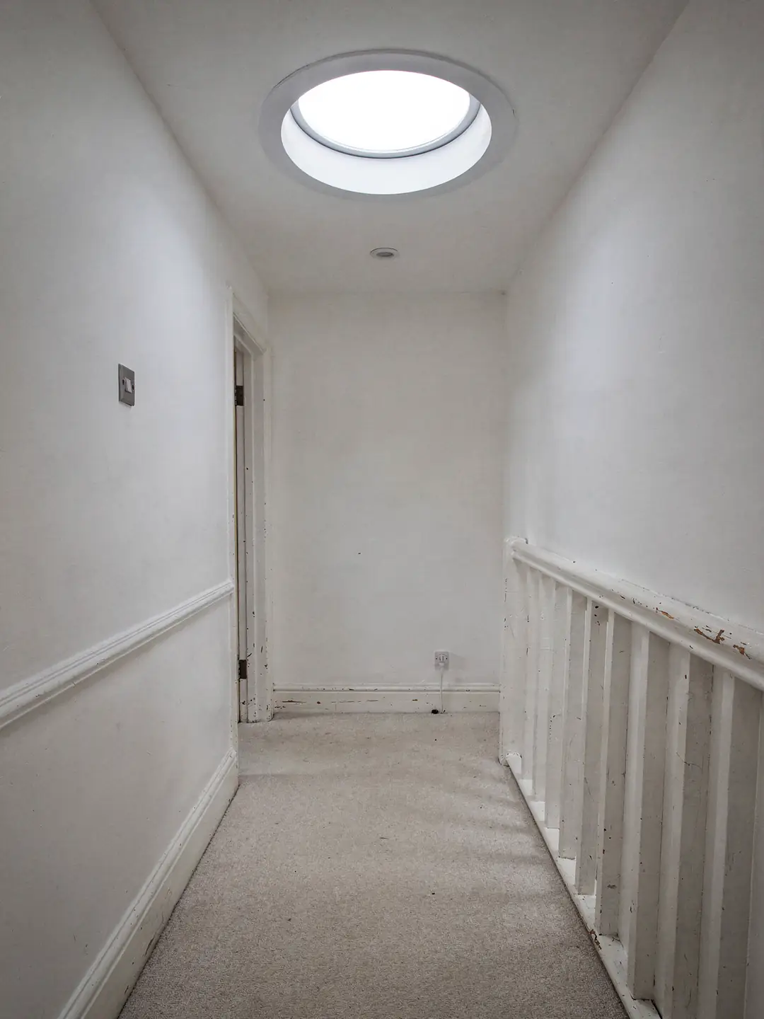 Round ceiling diffuser of a sun tunnel lighting a narrow upstairs landing with no windows
